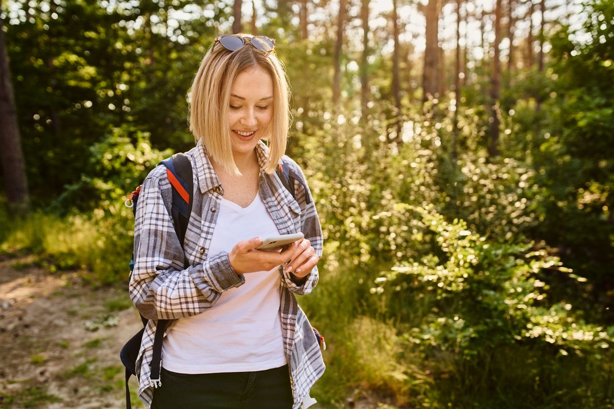 Young woman using mobile phone while walking in the woods during a hike.