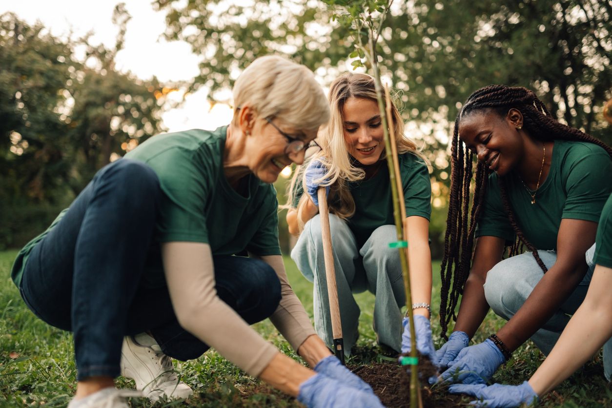 Three volunteers in green shirts plant a tree in the park, smiling and working together.