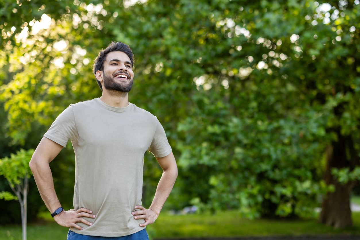 Young man stands confidently in a park.